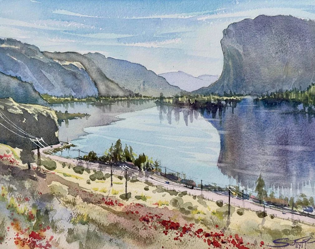 Watercolour painting of a view of mountains receding into the distance, a tall rocky bluff casting a huge reflection in the glassy mirror-like surface of Vaseux lake below.  painted from high on a hilltop, the foreground below shows the red sumac dotted along above the highway with cars and trucks driving by. Reds, Ochres, Blue water and sky.